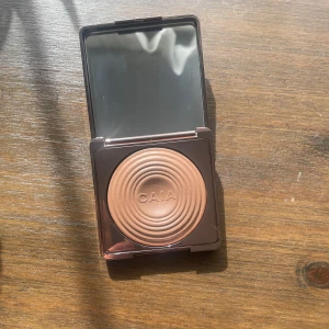 CAIA Glow Bronzer I färgen La Digue - Snygg bronzer från CAIA i nyansen La Digue. Kommer i en lyxig brun metallic-förpackning med spegel och har en pressad, cirkulär design. Den är öppnad men inte använd eller provad. Fick den i present för nån vecka sedan, säljer på grund av fel färg och går inte att skicka tillbaka då den är öppnad. Nypris 395 kr 