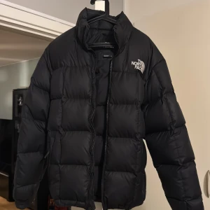 Svart pufferjacka från The North Face - Säljer en svart pufferjacka från The North Face med klassisk logga på bröstet. Jackan är vadderad och har hög krage, dragkedja framtill och quiltad design. Perfekt för kalla dagar och riktigt snygg streetstil. Det är storlek XS men funkar också som S då den är lite stor i storleken och man kan justera hur man vill att den ska sitta på just dig. 