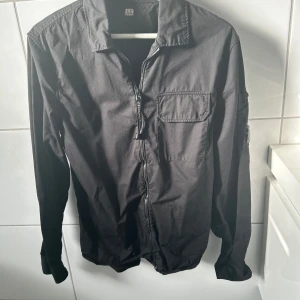 CP Company - CP company i klassisk svart, 100 % äkta. För att bevisa äktheten finns en QR-kod på en av bilderna. QR-koden är dock täckt i annonsen för att forhindra att den blir ogiltig om flera skannar den. Skicka ett meddelande om du är intresserad, så skickar jag koden direkt till dig! Detaljer: • Marke: C.P Company • Färg: svart • Storlek:S • Skick: 10/10 • Material: Bekvamt och slitstarkt tyg. Overshirten ikoniska C.P company logo bricka på vänster ärm gör den igenkännbar och ger en exklusiv touch.