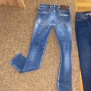 Replay Anbass slim fit  jeans blå, stl 28 - Säljer ett par Replay Anbass jeans i blå tvätt med snygga slitningar och skinny fit. Klassisk femficksmodell med läderpatch bak och dragkedjegylf. Jeansen är i stretchigt denim för en bekväm passform och har en modern look.