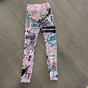 Stronger tights ice cream collection  - Färgglada tights från Stronger med tryck i rosa, blått, svart och gult. Hög midja med logotyp i midjeresåren. Materialet är stretchigt och passar perfekt för träning. Snygga detaljer med text och serietidningsgrafik över hela byxan.