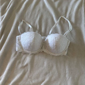 Vit spetsig bh från Lindex - Säljer en vit bh från Lindex i storlek 75C. Baksidan har hysk- och hakknäppning och spetsdetaljer längs kanterna för en extra feminin look.