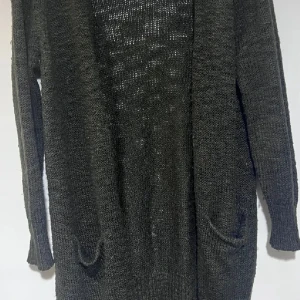 Mörkgrå stickad kofta från Gina Tricot - Lång, mörkgrå stickad kofta från Gina Tricot med öppen front och två fickor framtill. Koftan har en loose passform och är perfekt att slänga över en t-shirt eller topp. Materialet är grovstickat och ger en chill vibe.