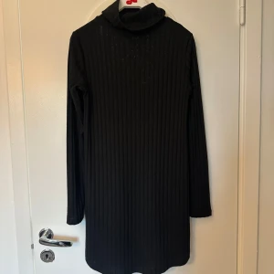 Svart ribbad klänning Gina Tricot - Svart ribbad klänning från Gina Tricot med polokrage och långa ärmar. Klänningen är kort och har en slim passform som sitter snyggt på kroppen. Perfekt för dig som gillar en enkel men stilren look.