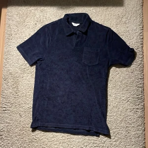 Mörkblå frotté piké från East West - Snygg mörkblå t-shirt från East West i frotté med klassisk krage och bröstficka. T-shirten har korta ärmar och en relaxed vibe, perfekt för chill dagar. Materialet är mjukt och ger en unik look. Bara att skriva om du har några frågor! Pris kan diskuteras vid snabb affär. 