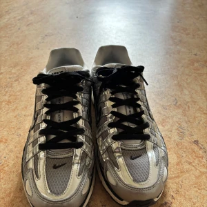 Nike P-6000 silver sneakers - Nike P-6000 sneakers i metallic silver och grå med svarta detaljer och snörning som jag bytte ut från de orginella vita. Ovandelen är i mesh och syntetmaterial med coola reflekterande paneler och svart swoosh på sidan. Skorna har en chunky vit och svart sula som ger en sportig vibe. om du köper de kan du få rabatterade priser på andra plagg