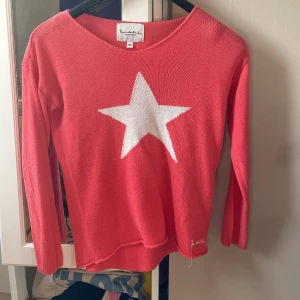 Korallröd stickad tröja med stjärna - Superfin korallröd stickad tröja från Bondelid med en stor vit stjärna på bröstet. Tröjan har rund halsringning och långa ärmar. Perfekt för dig som vill sticka ut lite extra med en cool detalj framtill.