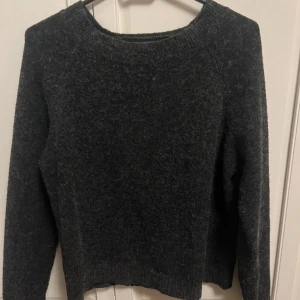 Mörkgrå stickad tröja från Vero Moda - Mysig mörkgrå stickad tröja från Vero Moda med rund halsringning och långa ärmar. Perfekt för kyliga dagar och enkel att matcha med jeans eller kjol. Tröjan har en klassisk, rak passform och är superbekväm att bära.
