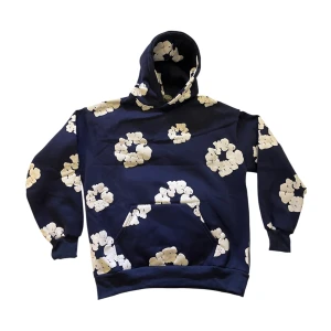 Blå Denim Tears Hoodie - Snygg marinblå hoodie från Denim Tears med stora vita blommor över hela tröjan. Klassisk känguruficka framtill och huva. Perfekt för dig som vill sticka ut med en unik streetwear-look. Skulle säga att den är mer M/L i storleken