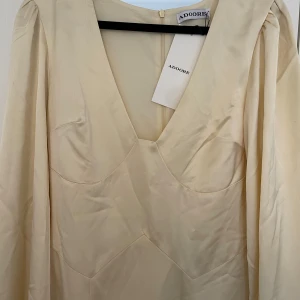 Adoore Andora långklänning vaniljgul - Säljer en elegant långklänning från Adoore i mjuk vaniljgul nyans. Klänningen har v-ringning, långa puffärmar och markerad midja. Tillverkad i ett glansigt material som ger en lyxig känsla. Helt oanvänd 💛