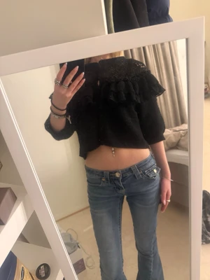 Svart croppad blus med volang - Svart croppad blus med volangdetaljer och spets upptill. Blusen har trekvartsärm och en lös passform, perfekt för en trendig look. Snygg och unik topp som sticker ut med sina detaljer. Det finns dock katt hår på toppen