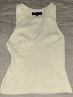 Vit v-ringad linnetopp från Zara - Snygg vit linnetopp från Zara med v-ringning och figurnära passform. Toppen är ärmlös och har en stilren, enkel design som passar perfekt till jeans eller kjol. Materialet känns mjukt och bekvämt mot huden.