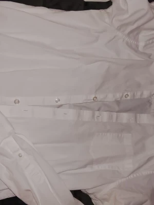 Vit skjorta från Pier One - Klassisk vit skjorta från Pier One med knappar framtill och krage. Skjortan är tillverkad i bomull och har lång ärm med knapp vid manschetten. Perfekt basplagg för garderoben.