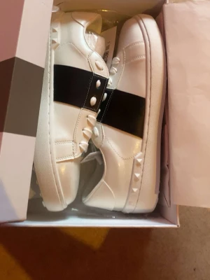 Valentino skor  - Pris kan diskuteras! Valentino Garavani Open sneakers i vitt med svart logoband och ikoniska Rockstud-detaljer. Klassisk och stilren modell som passar både till vardag och mer uppklädda outfits. Skorna är i fint skick och levereras med originalkartong, skosnören och skyddspapper. 