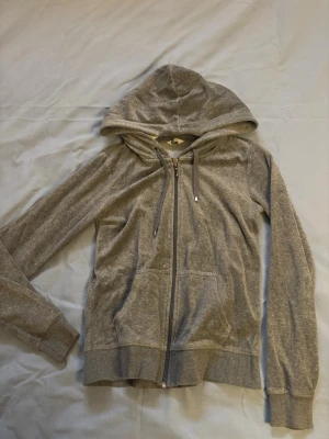 Grå zip hoodie med fickor - En enkel och stilren grå hoodie med dragkedja framtill och två stora fickor. Hoodien har justerbar huva med snören och ribbade muddar vid ärmar och nederkant. Perfekt för en avslappnad look och passar till det mesta.