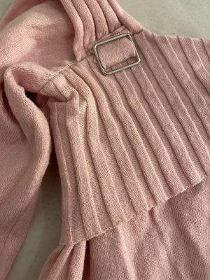 Ljusrosa stickad off shoulder-tröja - Trendig ljusrosa stickad tröja med off shoulder-design och bred ribbad kant upptill. Snygg detalj med silverfärgat spänne på axeln. Mjuk och skön kvalitet, perfekt för en stilren look.