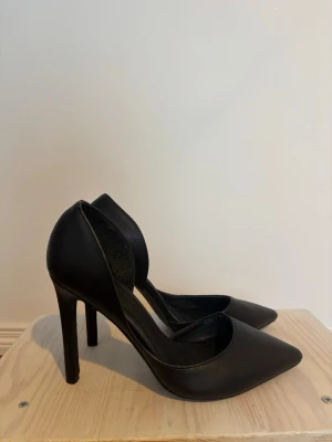 Svarta pumps med spetsig tå från NLY - Stilrena svarta pumps från NLY med spetsig tå och hög klack. Skorna är tillverkade i syntetmaterial och har en klassisk, elegant form som passar till många olika looks. Perfekta för dig som vill ha en tidlös och trendig sko.