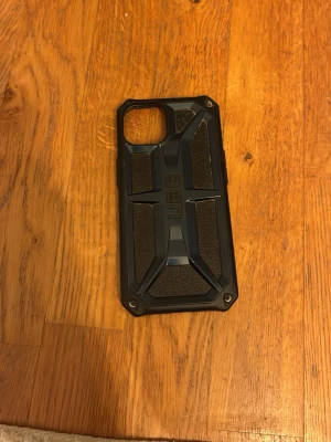 Svart UAG mobilskal med robust design - Säljer ett svart mobilskal från UAG med en robust och skyddande design. Skalet har en hård yta med detaljer i plast och gummi, samt förstärkta hörn och en cool, industriell look. Perfekt för dig som vill ha extra skydd till din mobil och gillar en tuff stil.