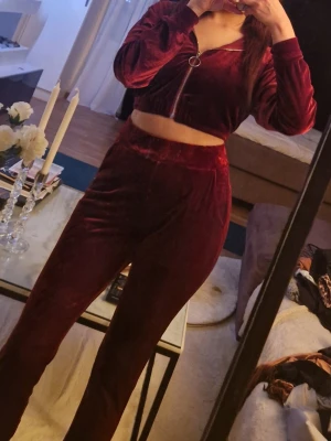 Vinrött vel soploungewear-set - Mysigt loungewear-set i vinröd sammet med croppad ziptröja och matchande höga byxor. Tröjan har dragkedja framtill och långa ärmar. Perfekt för chill dagar hemma eller när du vill vara bekväm men ändå snygg.