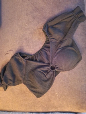 Svart topp  med ringdetalj - Trendig svart topp med ribbad struktur och  snygg ringdetalj framtill som ger en unik look. Perfekt för dig som vill sticka ut.