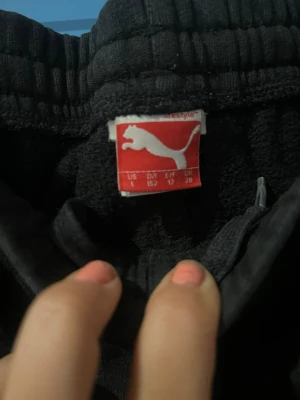 Svarta mjukisbyxor från Puma - Svarta mjukisbyxor från Puma med resår i midjan och vid bensluten. Byxorna har sidofickor och en liten Puma-logga på ena benet. Perfekta för en avslappnad stil och riktigt sköna att ha på sig.