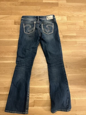 Blå bootcut jeans från Silver Jeans - Snygga blå bootcut jeans från Silver Jeans med dekorativa sömmar på bakfickorna. Klassisk femficksmodell i jeansmaterial och normal passform. Perfekta för dig som gillar en avslappnad men trendig look.