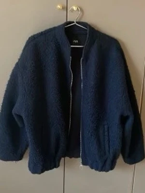 Mörkblå teddyjacka från Zara - Mysig mörkblå teddyjacka från Zara med dragkedja framtill och två fickor. Jackan har en avslappnad passform och är perfekt för kyliga dagar. Tillverkad i mjukt teddy-material som håller dig varm och bekväm.