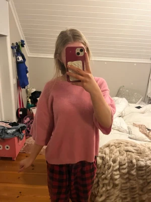 Rosa stickad tröja med kort ärm - Mysig rosa stickad tröja med avslappnad passform och korta ärmar. Tröjan har rund halsringning och ribbade kanter. Perfekt för lager-på-lager och en chill look.