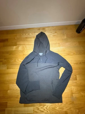 Grå hoodie från Studio Total - Snygg grå hoodie från Studio Total med halv dragkedja och justerbar huva. Tillverkad i mjukt material och har en praktisk ficka med dragkedja på sidan. Perfekt för en avslappnad och stilren look.