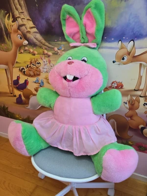 Stor grön och rosa kaninnalle - En jättestor mjuk kanin i plysch med grön kropp och rosa detaljer. Kaninen har stora öron med rosa insida, en rosa nos och mage samt en rosa tyllkjol och rosett på huvudet. Perfekt som dekoration eller gosedjur i barnrummet.