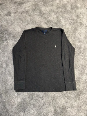 Mörkgrå långärmad tröja Polo Ralph Lauren - Säljer en mörkgrå långärmad tröja från Polo Ralph Lauren med diskret logga broderad på bröstet. Tröjan har rund halsringning och är tillverkad i ett mjukt, ribbat material som ger en avslappnad och stilren look. Storlek S, skriv om du har frågor och lägg gärna bud!
