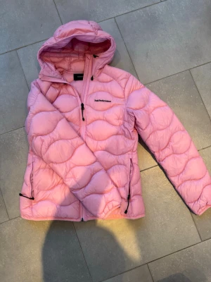 Rosa dunjacka Peak Performance M NYSKICK - Säljer en rosa dunjacka från Peak Performance med huva och dragkedja framtill. Jackan har quiltad design, två sidofickor med dragkedja och en bröstficka. Perfekt för kalla dagar och riktigt snygg färg som sticker ut.