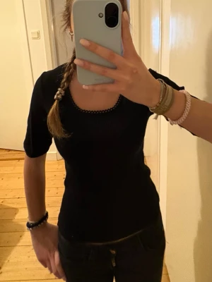 Svart trekvartströja - En svart ribbad trekvarts ärmad tröja med små volanger på ärmarnas slut och i halsen. Använd men inga synliga märken eller skavanker.  Säljer då ja inte använder den.