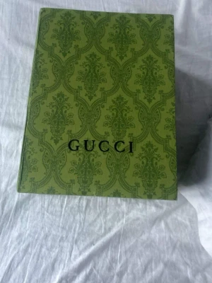 Brun keps med GG-mönster från Gucci - Säljer en brun keps från Gucci med det klassiska GG-monogrammet över hela kepsen. Kepsen har böjd skärm och justerbar rem bak. Kommer med originalbox och tags. Perfekt för dig som vill ha en exklusiv och trendig accessoar.ny pris 4200