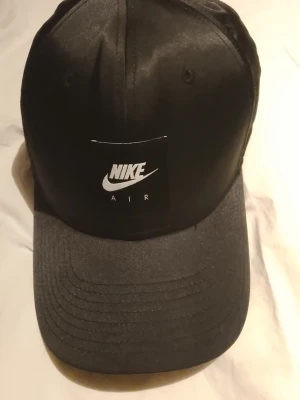 Svart keps från Nike Air - Snygg svart keps från Nike Air med klassisk böjd skärm och broderad logotyp framtill. Kepsen har en stilren design och justerbar passform baktill. Perfekt accessoar för en sportig och trendig look.