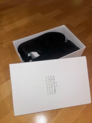 Svarta sneakers från Maison Margiela - Stilrena svarta sneakers från Maison Margiela med klassisk siluett. Skorna har ovandel i skinn och mocka, samt snörning framtill. Perfekta för dig som gillar minimalistisk och clean design.