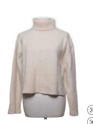 Vit polotröja i stickat material - Klassisk vit stickad polotröja med hög krage och avslappnad passform. Tröjan har långa ärmar och ribbstickade detaljer vid krage, ärmslut och nederkant. Perfekt för lager på lager och en clean look. Materialet ser mjukt och fluffigt ut.