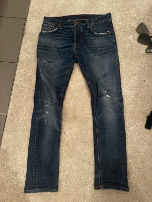 Blå jeans från Nudie Jeans - Säljer ett par Nudie grim Tim Jeans med snygga slitna detaljer som är fixade. Passar perfekt på mig som är 180 och väger 67kg. Skriv vid funderingar!
