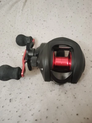 Svart och röd multirulle till fiske - Säljer en svart multirulle med röda detaljer och två greppvänliga handtag. Rullen har en modern design och är tillverkad i metall och plast. Perfekt för dig som gillar sportfiske och vill ha bra kontroll på kastet.