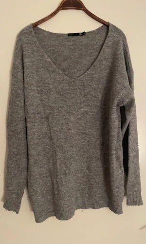 Grå stickad v-ringad tröja  - Mysig grå stickad tröja med v-ringad hals och långa ärmar. Perfekt för att hålla sig varm under kyliga dagar. Tröjan har en enkel och stilren design med ribbade muddar vid ärmslut och nederkant.