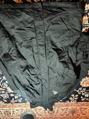 Svart Adidas pufferjacka herr L  - Svart pufferjacka från Adidas i storlek M. Jackan har quiltad design, lång ärm och dragkedja framtill. Materialet är polyester och jackan har en klassisk Adidas-logga på bröstet. Perfekt för kyliga dagar och har en sportig vibe.