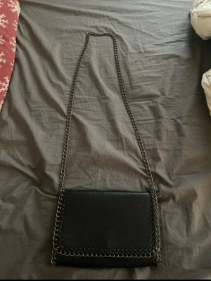 Svart axelväska med kedja - Kedjeväska. Bra skick förutom att kedjan är lite missfärgad på vissa ställen som man ser på bilderna, samt att jag råkade spilla bronzer inuti.