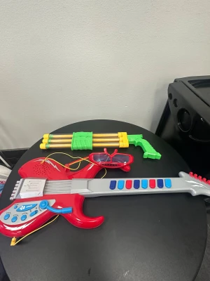 Ingen väst på bilderna - Det finns ingen väst på bilderna, endast leksaksgitarr, leksaksglasögon och leksakspistol. Ingen information om väst, färg, märke eller material kan ges.