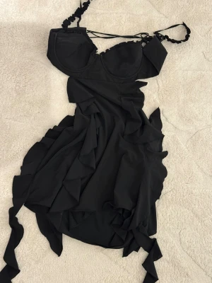 Svart volangklänning Oh Polly - Supersnygg svart kortklänning från Oh Polly med volangdetaljer och figurnära passform. Klänningen har bygelkupor, smala axelband med snörning och dragkedja i sidan. Perfekt för dig som vill ha en trendig och feminin look. Öppen för byte av annan klänning från hp. Perfekt inför nyår eller festklänning