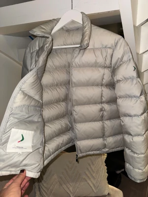 Cremevit dunjacka från Boomerang XL - Säljer en lättvikt dunjacka från Boomerang i storlek XL, men modellen är liten i storleken och passar bäst för dig som brukar ha 40–42. Se bifogade bilder med mått för säkerhets skull.  Jackan är i mycket fint skick och är precis tvättad. Inga defekter. Jackan har quiltad design, hög krage och dragkedja framtill. Yttertyg och foder är i nylon, fyllningen består av 90% dun och 10% fjäder. Perfekt för kalla dagar och har en clean, modern look.