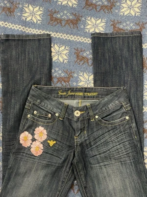 Guess Jeans Pismo Straight med broderi - Mörkblå jeans från Guess, modell Pismo Straight, med raka ben och gul kontrastsöm. Framtill finns broderade rosa blommor och ett bi, samt bi-broderier på bakfickorna. Jeansen har klassisk femficksdesign och är tillverkade i jeansmaterial. 