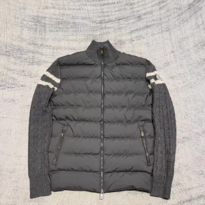 KÖP ELLER BYTE Grå dunväst från Moncler med stickade ärmar - Snygg grå dunväst från Moncler med stickade ärmar och vita ränder. Västen har dragkedja framtill, två fickor med dragkedja och Moncler-logga på ärmen. Perfekt för stilrena outfits Storlek L/M 