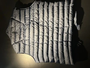 Mörkblå dunväst från J.Lindeberg - Snygg mörkblå dunväst från J.Lindeberg med quiltad design och vertikala sömmar. Västen har en hög krage, dragkedja framtill och logotypen tryckt på bröstet. Perfekt för lager-på-lager och chill stil under kyliga dagar.Nypris är 2200kr.