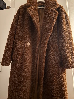 Brun faux fur jacka från Reserved - Mysig brun teddyjacka från Reserved i storlek 34. Jackan är lång , två stora fickor framtill och stängs med en knapp. Perfekt för kalla dagar och har en riktigt fluffig och trendig look.