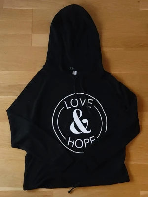 Svart tröja - Svart tunnstickad tröja med luva och tryck framtill. Tunn och skön tröja som är lätt att matcha med jeans eller strandkläder. 